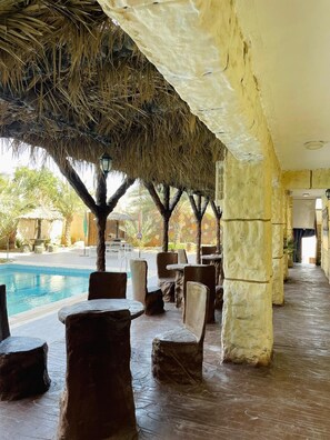 An outdoor pool area with thatched roofs, stone pillars, and lounge chairs. - Lafamilia Albadwan (Sweimeh)