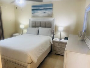 Habitación de hotel con cama, mesitas de noche, lámpara, reloj digital y un cuadro en la pared.