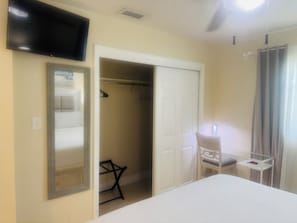 A hotel room with a bed, a TV mounted on the wall, a closet with a mirror, and a small table with a chair.
