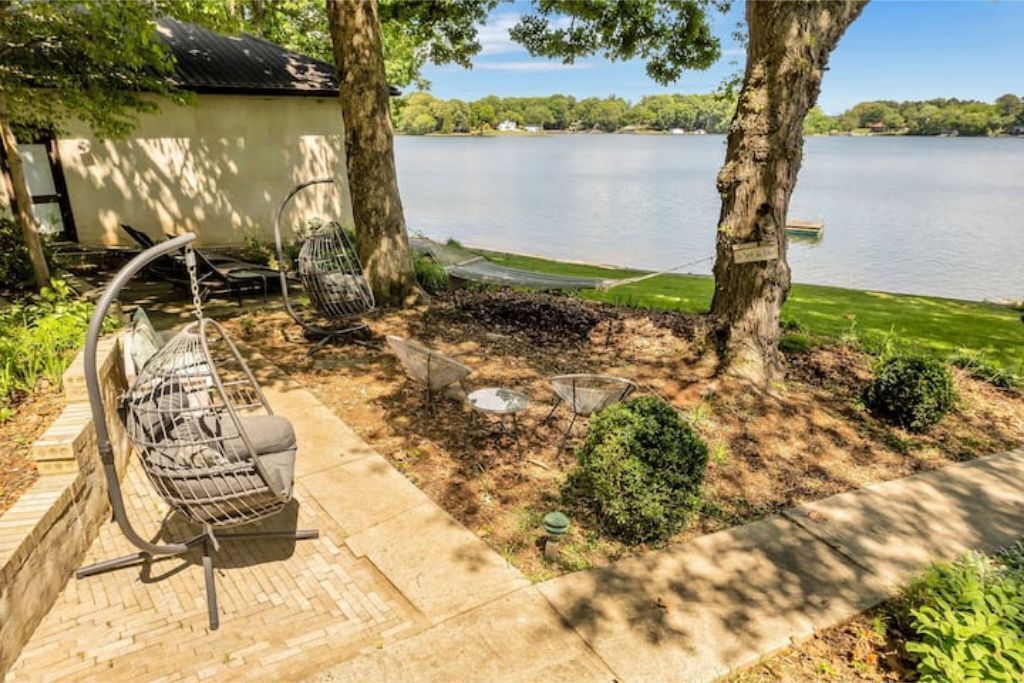 Un patio con una silla colgante, un hogar para fogata y vistas a un lago.