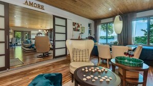 Ein modernes Interieur mit Holzbalkendecke, einer Sitzecke mit rundem Tisch und Blick durch große Fenster nach draußen.