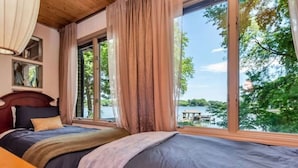 Ein Schlafzimmer mit großem Fenster, einem Bett, einem Nachttisch und einer Lampe.