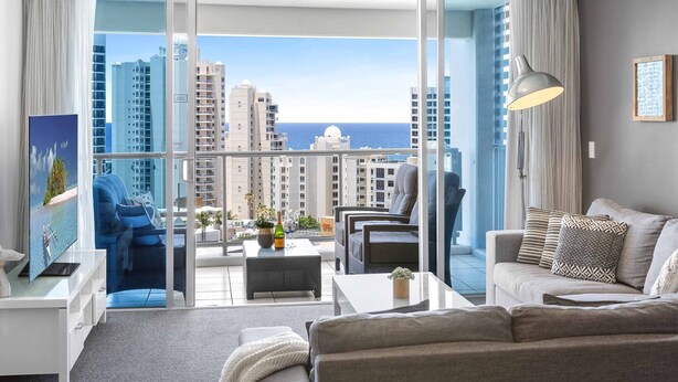 A modern living room with a balcony, furnished with a sofa, armchairs, and a coffee table. - Chevron Renaissance Ocean View (Surfers Paradise)