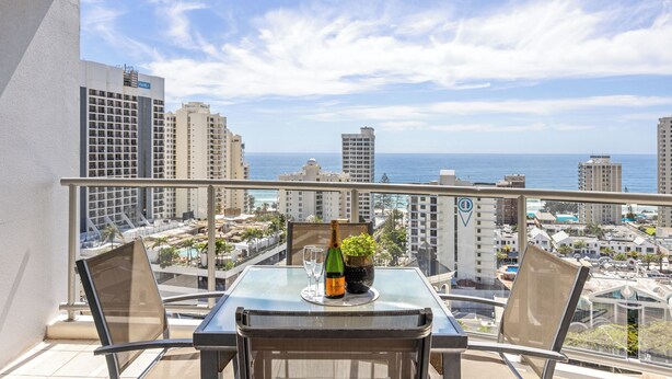 Een balkon met een tafel gedekt voor twee, met uitzicht op een stadslandschap en de oceaan.