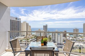 A balcony with a table set for two, overlooking a cityscape and the ocean. - Chevron Renaissance Ocean View (Surfers Paradise)