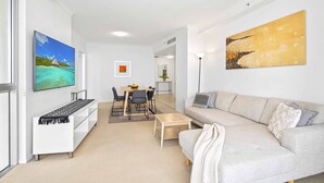 A modern living room with a sofa, coffee table, and a dining area with chairs and a table. - Chevron Renaissance Ocean View (Surfers Paradise)