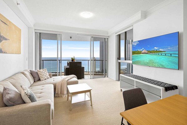 A modern living room with a sofa, a small table, and a TV displaying a tropical scene.