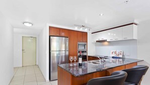 A modern kitchen with a central island, stainless steel appliances, and black bar-style chairs. - Chevron Renaissance Garden View (Surfers Paradise)