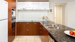 A modern kitchen with wooden cabinets, a granite countertop, a stainless steel sink, and a built-in oven. - Chevron Renaissance Garden View (Surfers Paradise)