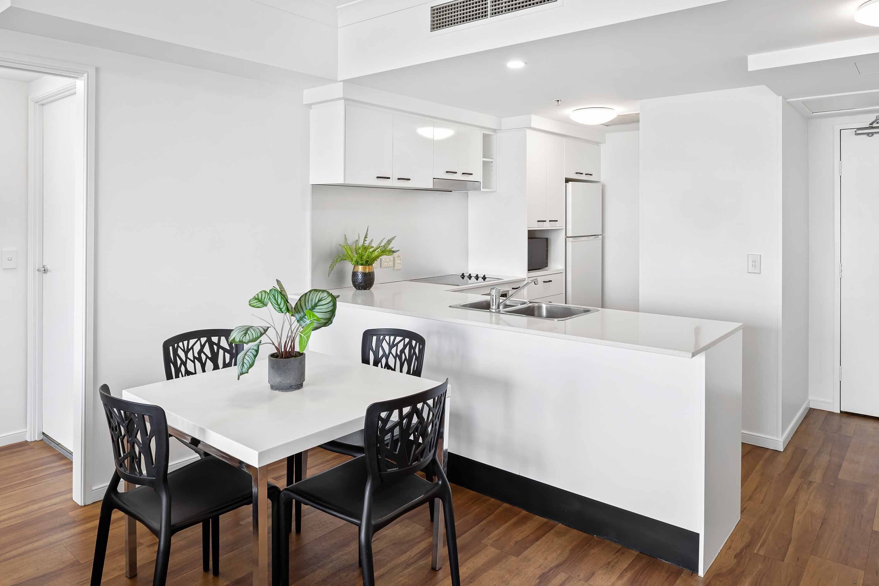 Een moderne keuken met witte kasten, een centraal eiland en zwarte stoelen.