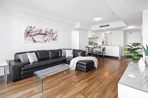 Uma sala de estar moderna com um sofá de couro preto, uma mesa de centro de vidro e um espaço de refeições com uma mesa e cadeiras brancas.