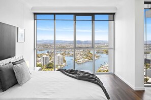Enjoy a panoramic city view from the comfort of this stylish bedroom, featuring a large window, a neatly made bed, and a framed picture.