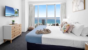 A bedroom with a bed, a dresser, a TV, and a large window with a view of the ocean. - Chevron Renaissance Ocean View (Surfers Paradise)