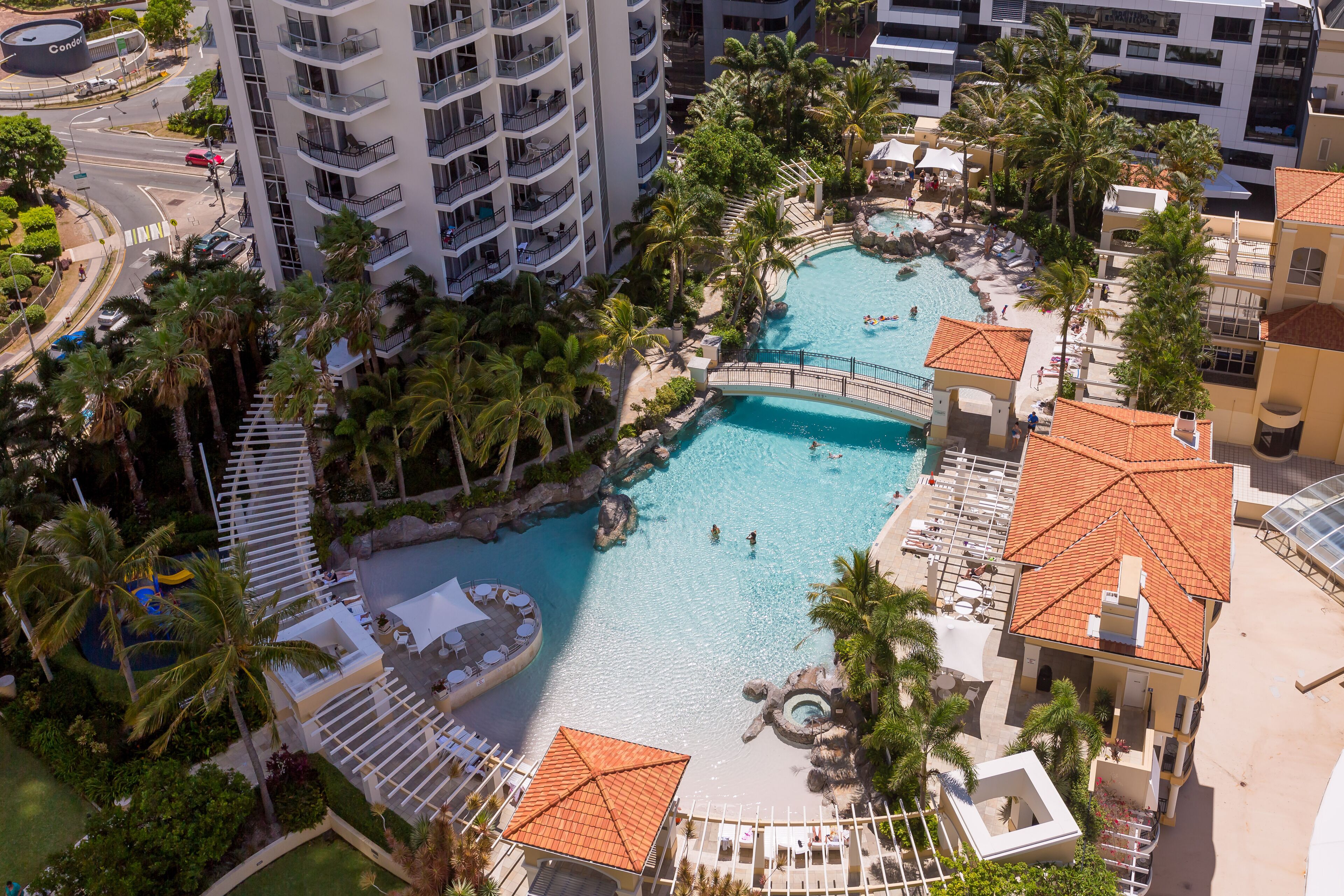 Een resort met een groot zwembad, palmbomen en uitzicht op een stadsbeeld.