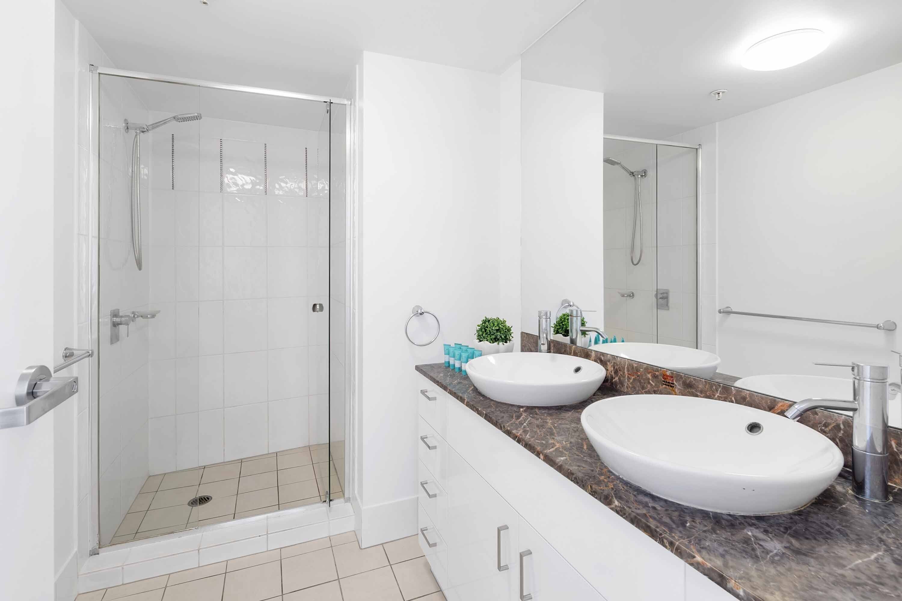 A modern bathroom with a glass-enclosed shower, two sinks, and a large mirror.