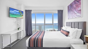 Habitación de hotel con una cama grande, televisor en la pared, escritorio y vistas al océano.