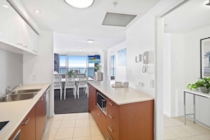 A modern kitchen with a central island, white cabinetry, and a view of the sea through large windows.