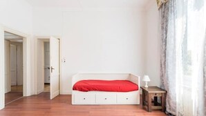 A bedroom with a white bed, a wooden floor, a small bedside table with a lamp, and a door leading to another room. - Country house, surrounded by greenery and nature. Great for relaxation (Camaiore)