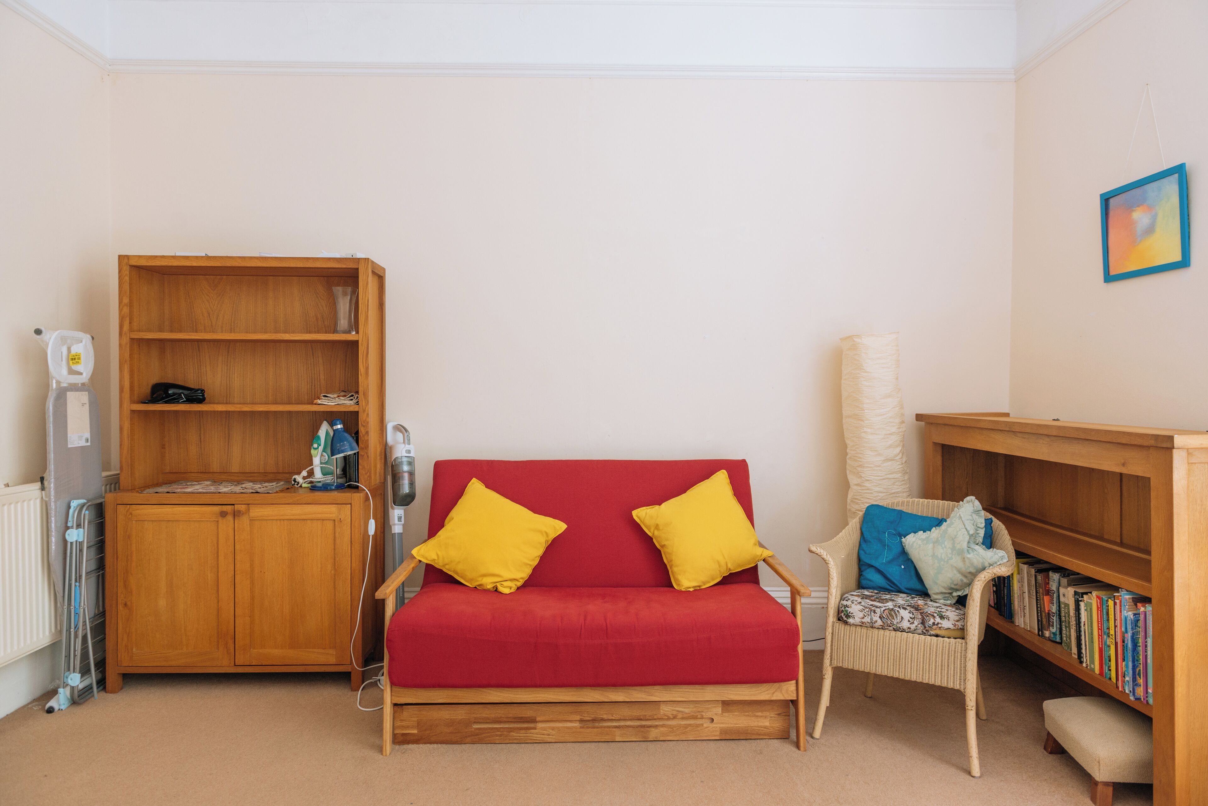 Um quarto aconchegante com um sofá vermelho, estantes de madeira e uma cadeira de vime.
