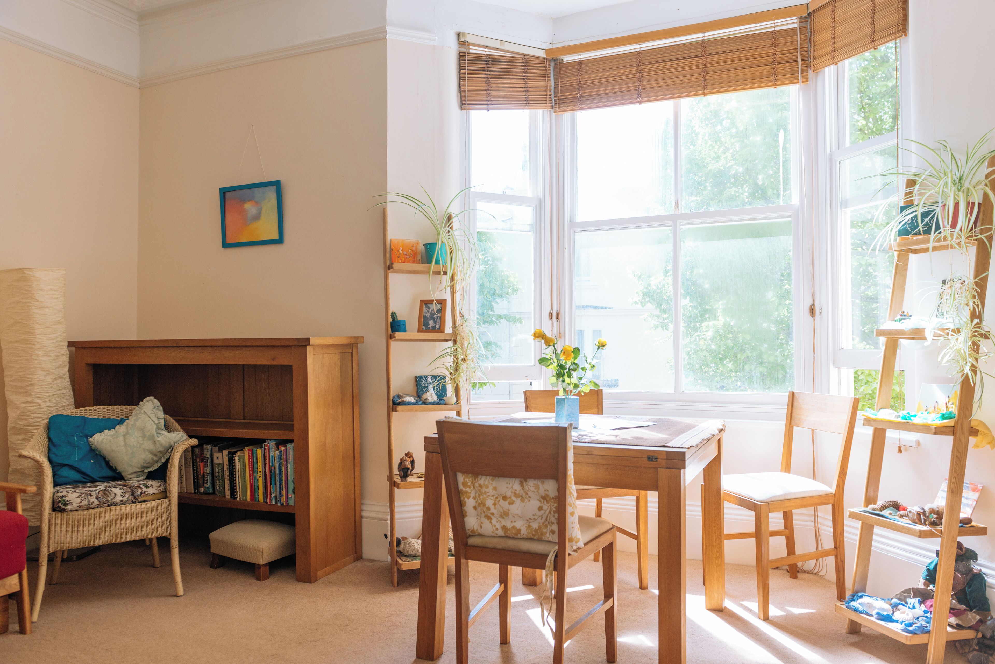 A cozy reading nook with a bookshelf, a chair, and a table by a large window.