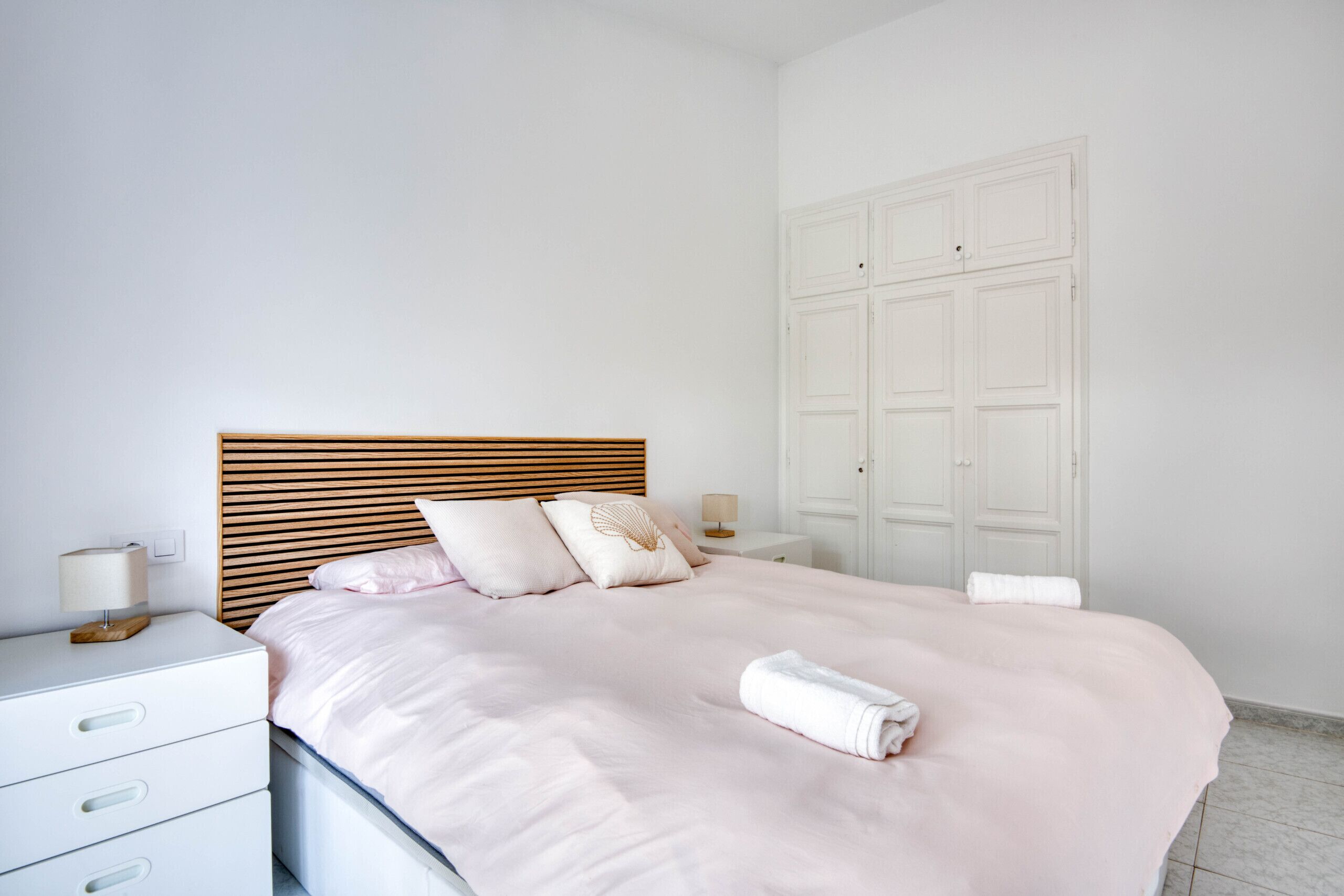 A neatly made bed with a wooden headboard, a bedside table with a lamp, and a white wardrobe.