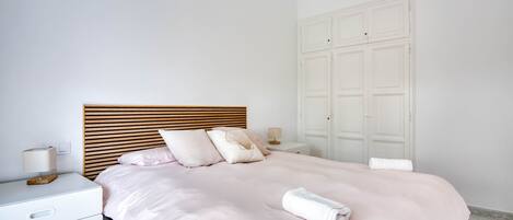 A neatly made bed with a wooden headboard, a bedside table with a lamp, and a white wardrobe.