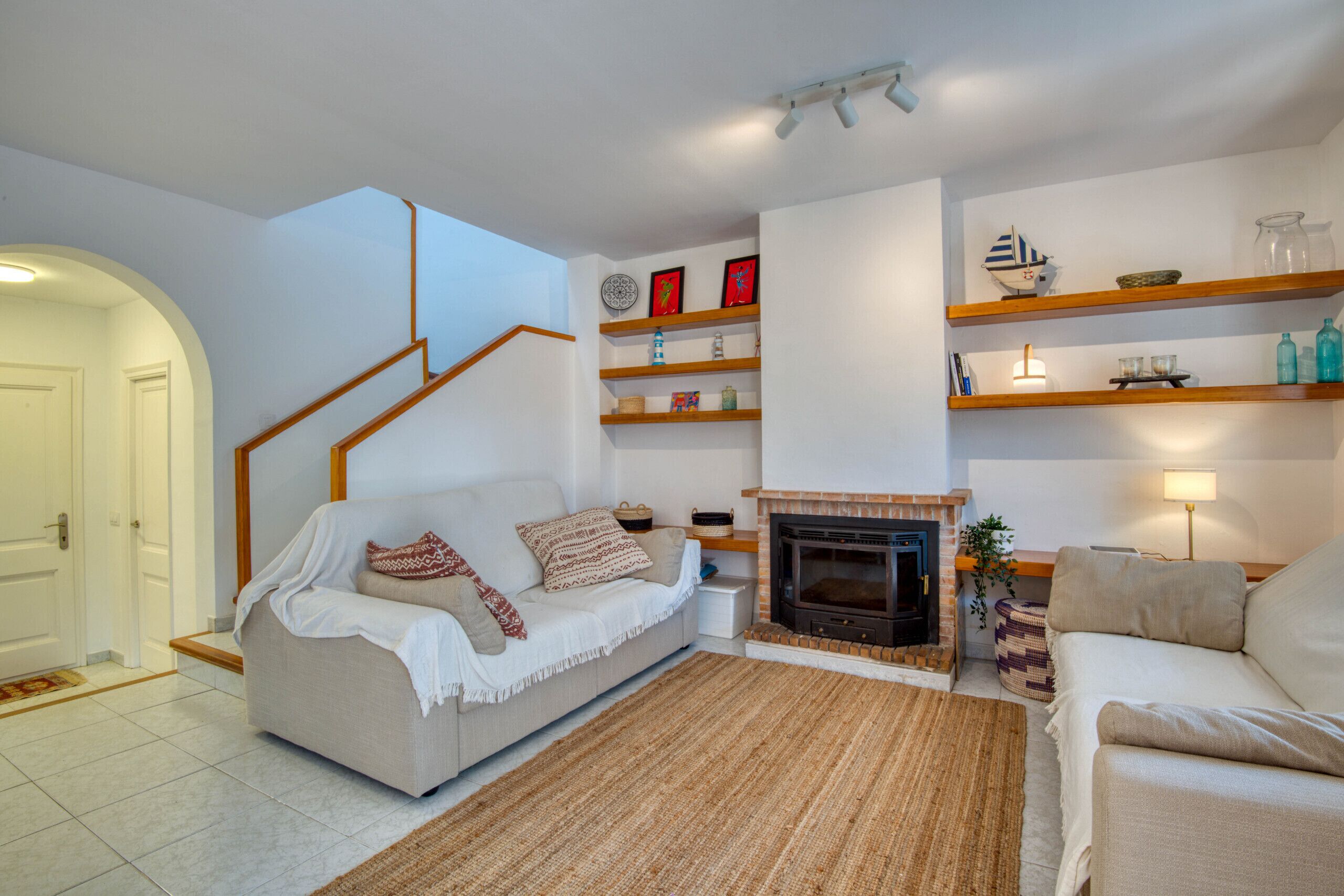Una sala de estar con escalera, chimenea y estantes decorados con objetos ornamentales.
