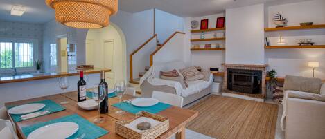 A modern living room with a dining area, wooden furniture, a fireplace, and a staircase.