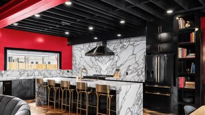 Une cuisine moderne dotée d’un îlot en marbre, de meubles de rangement noirs et de tabourets de bar dorés.