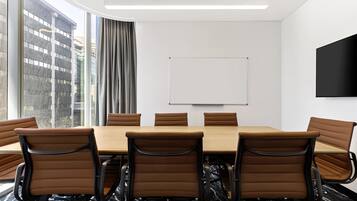 A conference room with a large table, six brown chairs, a whiteboard, and a TV on the wall.