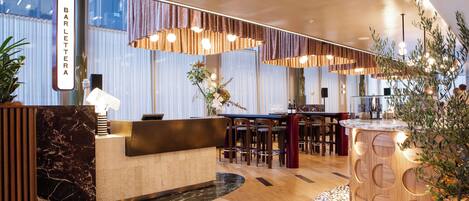 A modern hotel lobby with a reception desk, seating area, and decorative plants.