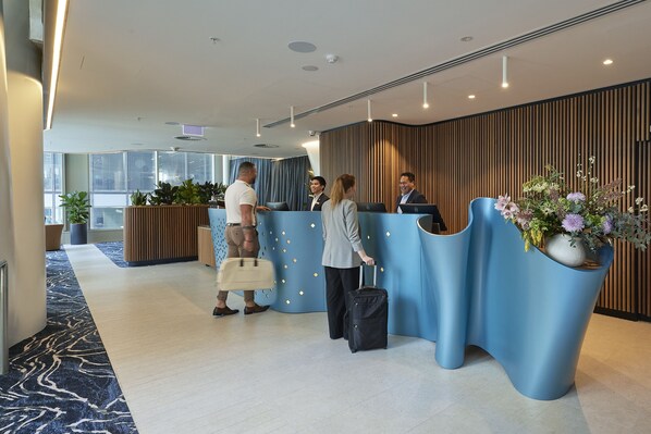 A reception area with a modern design, featuring a blue reception desk, a wooden panel wall, and potted plants. - Citadines Walker North Sydney (North Sydney)