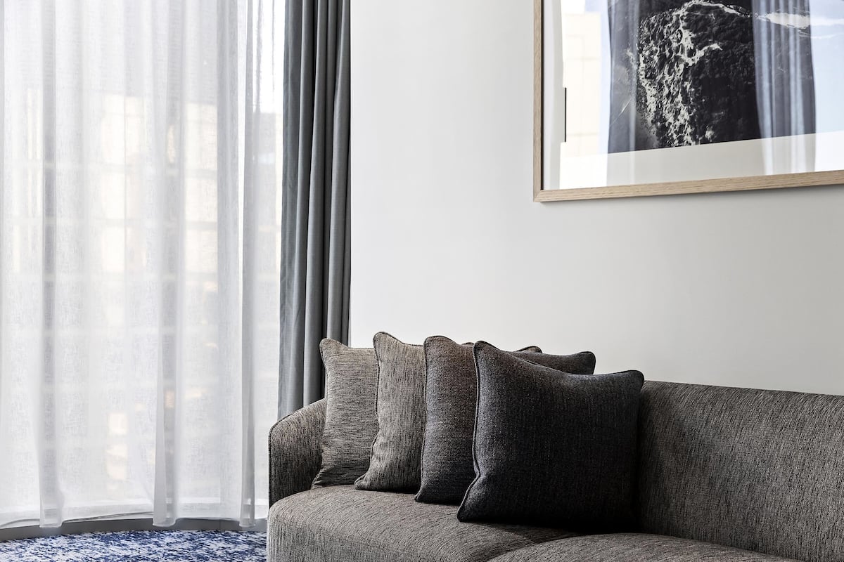 A modern living room with a grey sofa, a framed picture on the wall, and sheer curtains.
