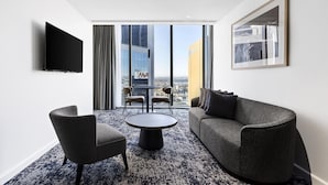 Una habitación de hotel moderna con un ventanal grande, un televisor de pantalla plana, una mesa de centro redonda, dos sillones y un sofá.