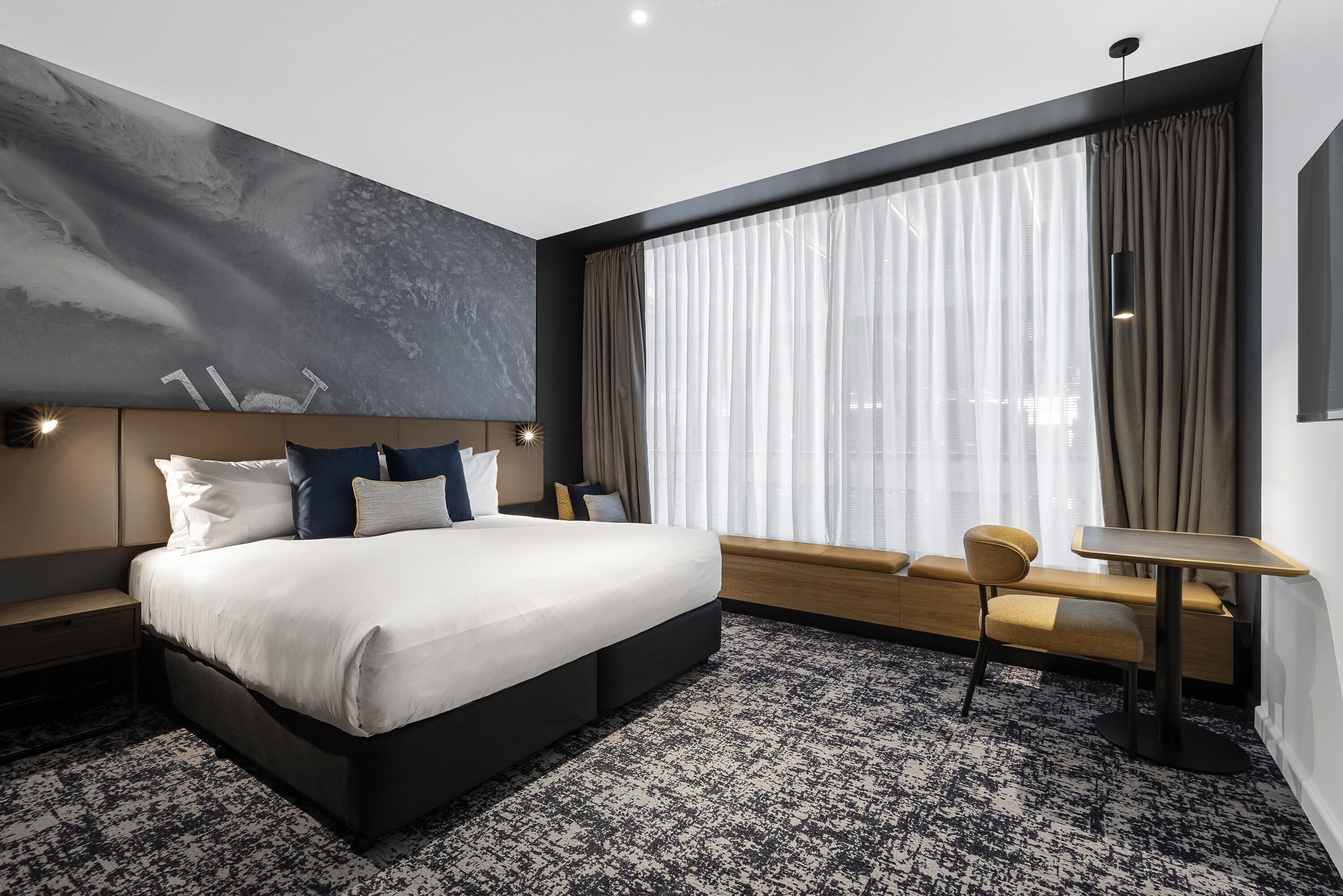 A modern hotel room with a large bed, a small table, and a bench.