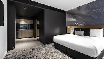 A modern hotel room with a large bed, a dark wall, and a painting of a mountain.