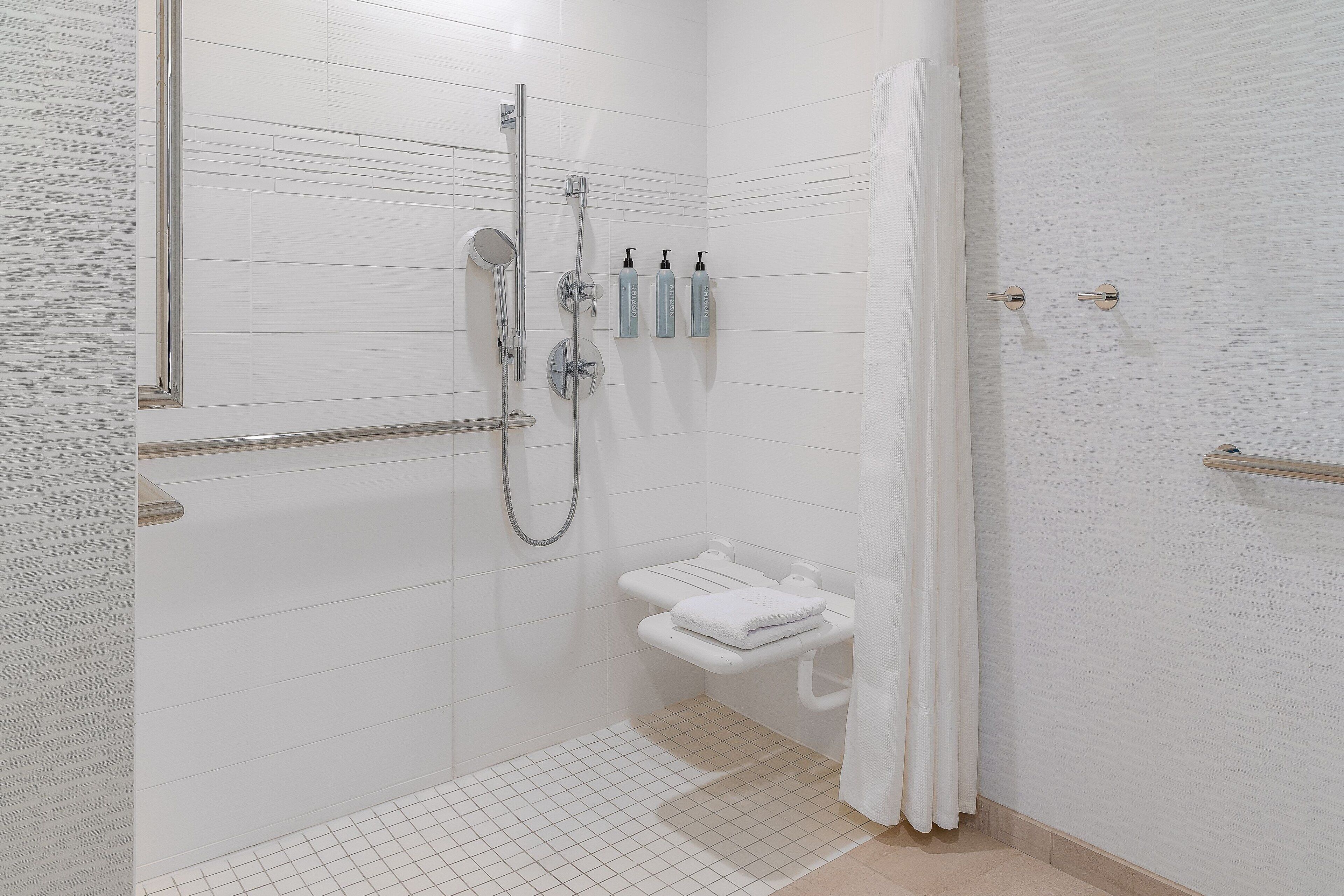 A modern bathroom with a walk-in shower, a toilet with a towel rack, and three toiletries on the wall.