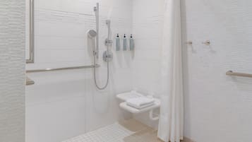 A modern bathroom with a walk-in shower, a toilet with a towel rack, and three toiletries on the wall.