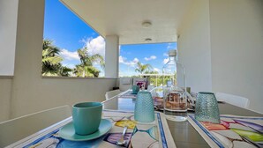 A dining table set with a bottle, glasses, and a cup, overlooking a garden with palm trees.