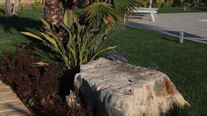 A landscaped garden with palm trees, a stone bench, and a white umbrella.