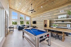 Relax in a spacious area with a pool table and comfortable seating, surrounded by high ceilings and large windows.