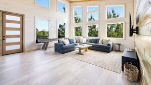 Un salon spacieux avec un grand canapé d’angle, une table basse et une vue sur les arbres grâce à de grandes fenêtres.