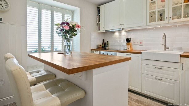 A modern kitchen with white cabinetry, a wooden countertop, and a built-in bench. - Luxurious 2-Bed Apartment - Jun-Aug Weekly Rate (Rathfarnam Dublin 14)