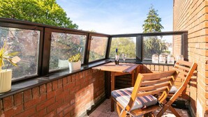 A corner patio with a wooden table and chairs, potted plants, and a view of trees and buildings. - Luxurious 2-Bed Apartment - Jun-Aug Weekly Rate (Rathfarnam Dublin 14)