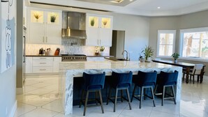 A modern kitchen with white cabinets, a marble island, and blue bar stools. - Resort Living Las Vegas (Las Vegas)