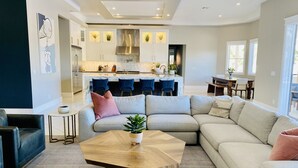 A modern living room with a large L-shaped sectional sofa, a wooden coffee table, and a kitchen area with bar seating. - Resort Living Las Vegas (Las Vegas)