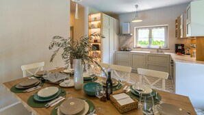 Een eetgedeelte met een houten tafel gedekt voor een maaltijd, een vaas met groene planten en een fles wijn.