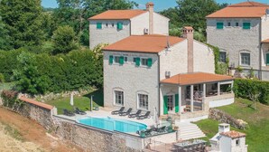 Een stenen villa met een zwembad, buitenzitplaatsen en een overdekt terras.