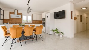 Une cuisine moderne avec des meubles blancs, un îlot central et un coin repas agrémenté de chaises orange.