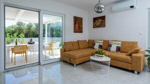 Un salon moderne avec un canapé marron, une porte en verre donnant sur un espace extérieur et une petite table d’appoint ronde, de couleur blanche.